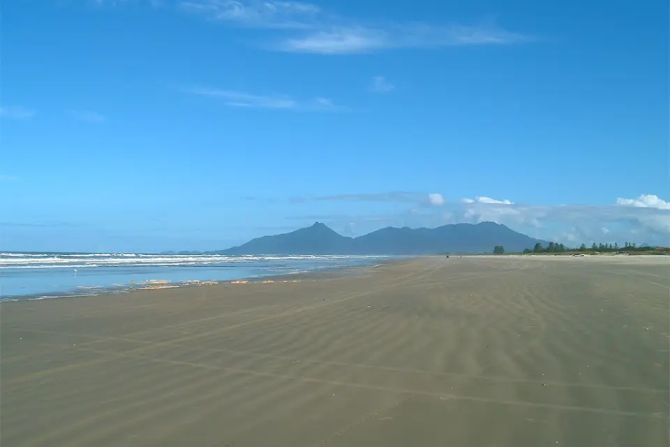 Faixa de areia extensa da praia de Ilha Comprida com a serra ao fundo