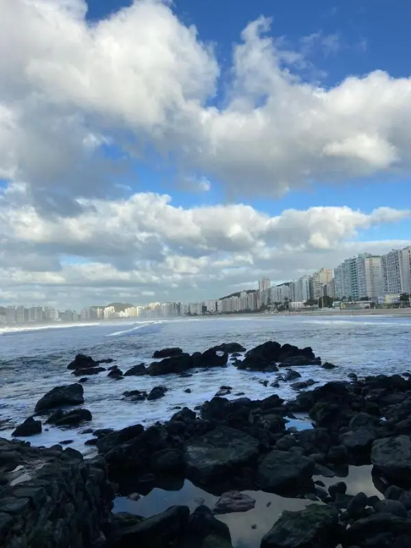 Costão rochoso e mar com a orla do Guarujá ao fundo