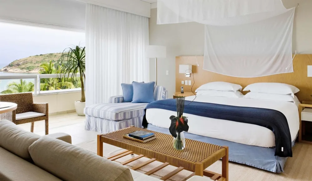 Suíte do Hotel Jequitimar com cama king, sala de estar e varanda com vista para o mar e o morro